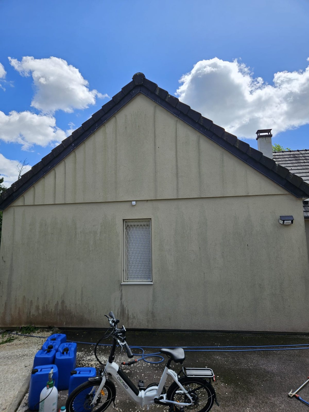 Avant : pignon verdâtre, des bidons et un vélo devant.