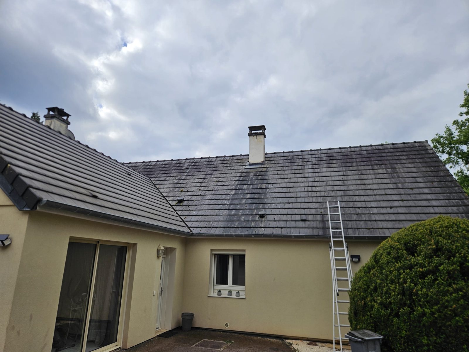 Avant : toiture grise d'une maison en L, tachée de mousse.